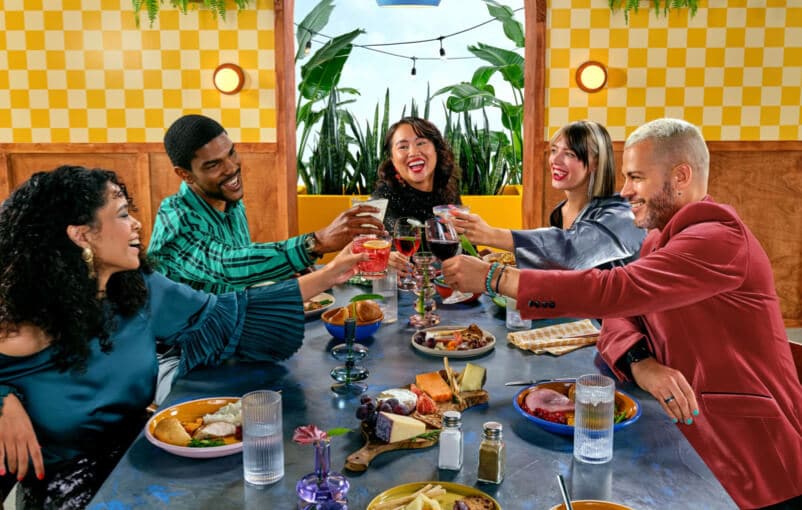 A group of five diverse people sitting around a table enjoying food and drink together.