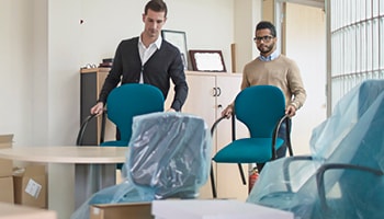 Two people moving chairs into an office. 