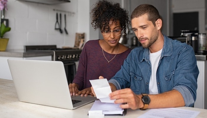 Young couple checking bills while managing accounts on home banking app.