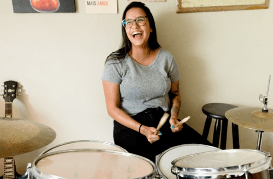 A woman smiling playing the drums