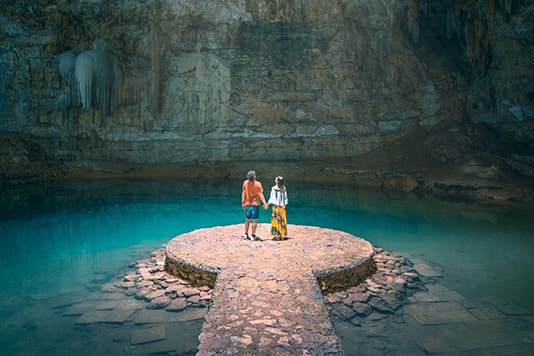 Two people holding hands inside a zenote cave lake in Mexico