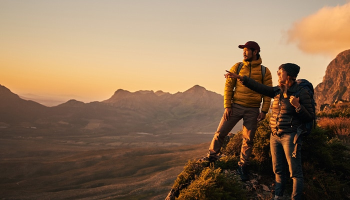 Two people on a cliff looking at the view during sunrise.