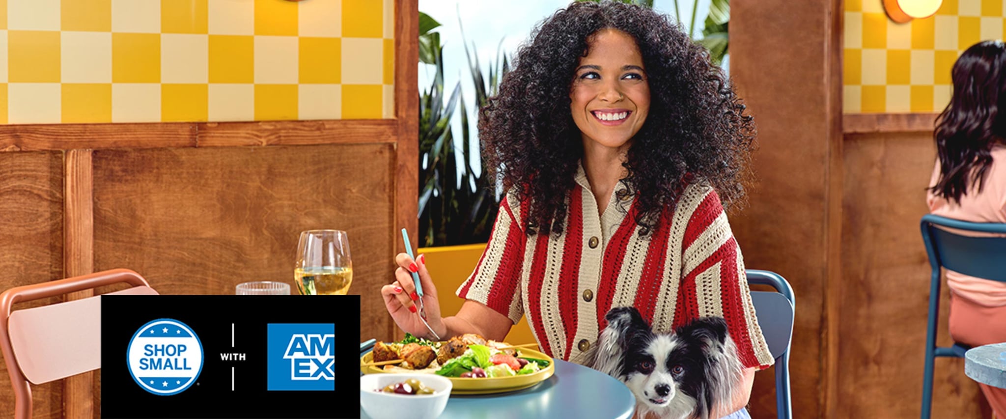 Woman sitting at table with dog in lap and eating food with wine