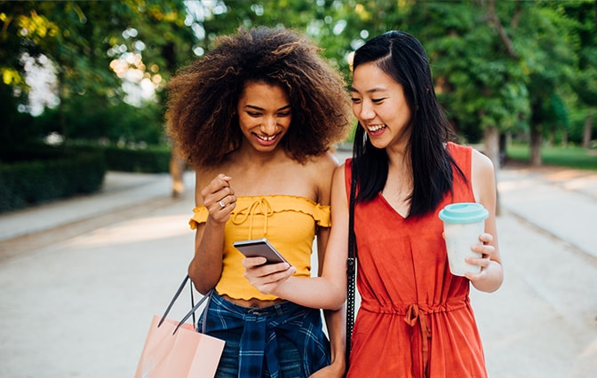 Two women walking and looking at phone while shopping