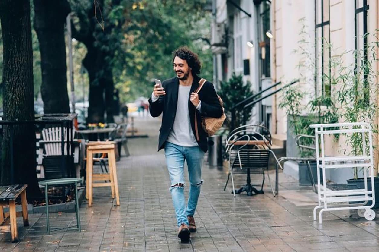 A man strolls down a street, holding a cup of coffee, enjoying his day while checking his credit score update on his phone.