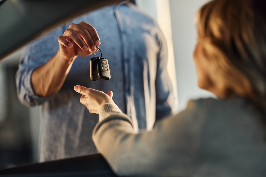 A driver being handed the keys through the window of a car