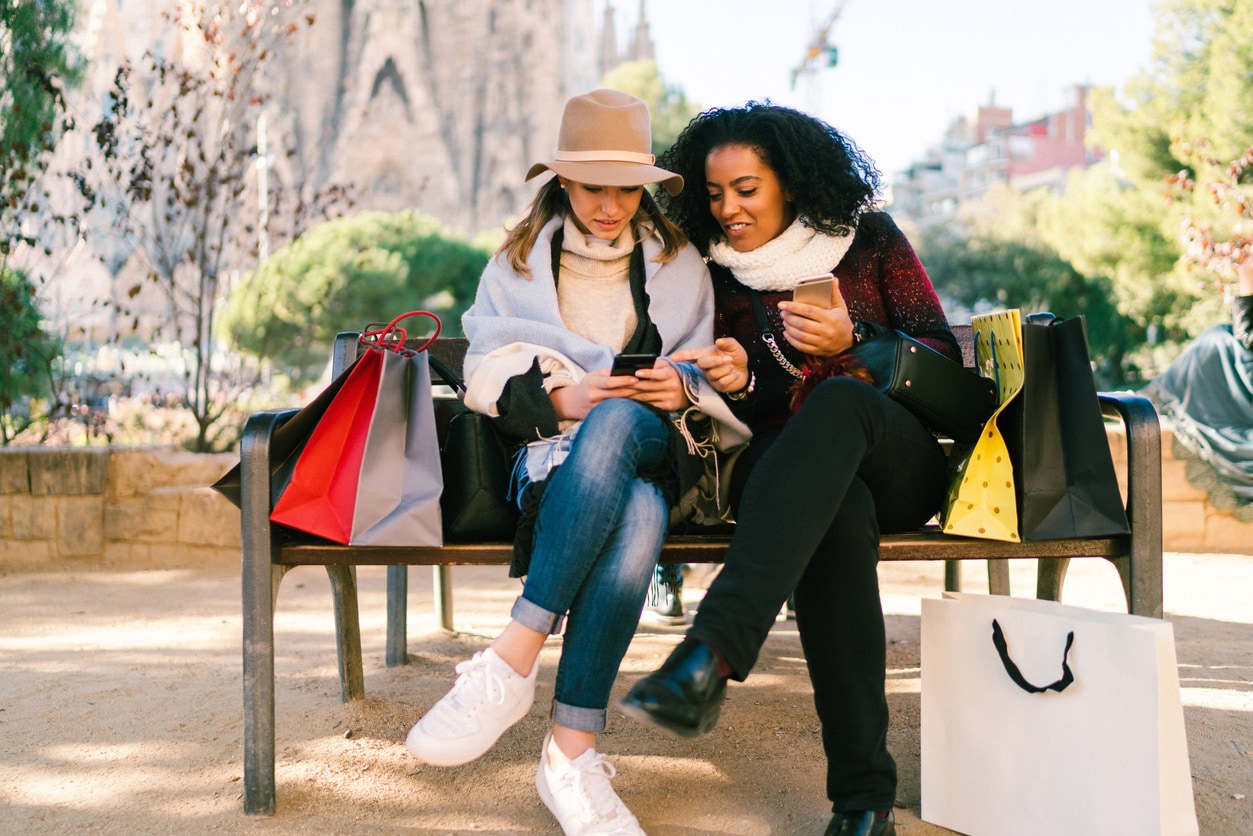 Two women sitting on a bench with shopping bags.