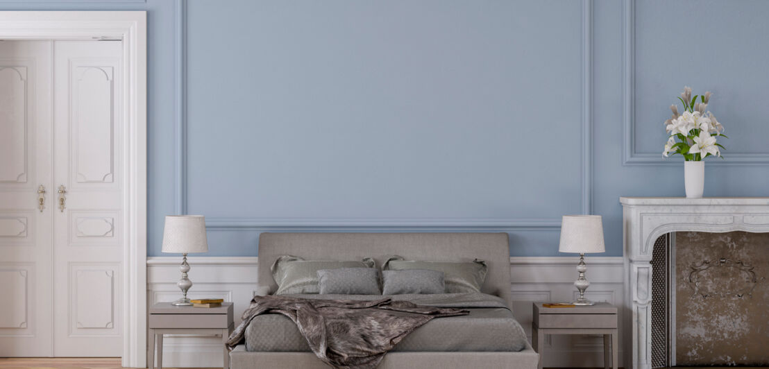 Ein elegantes Schlafzimmer mit einem grauen Doppelbett vor einer hellblauen Wand