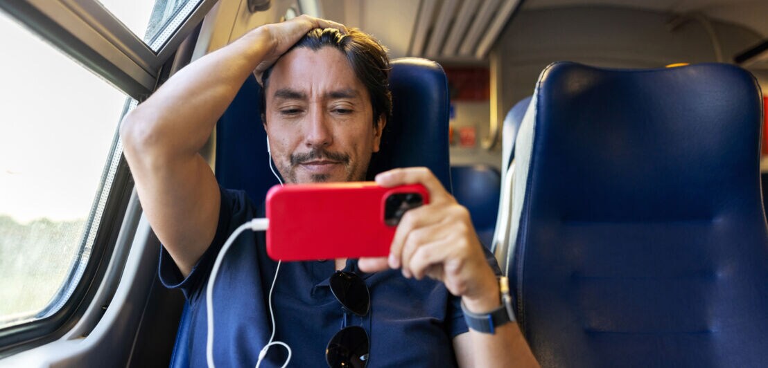 Ein Mann in einer Bahn mit Kopfhörern, der auf ein Smartphone schaut