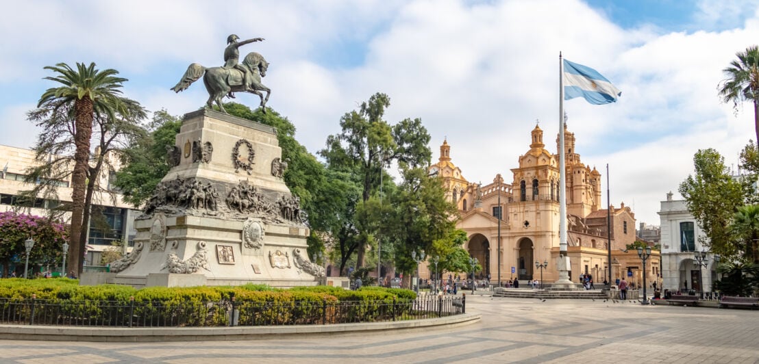 Reiterdenkmal auf einem Platz und argentinischer Flagge vor einer Kathedrale im Kolonialstil