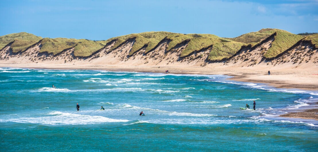 Strandabschnitt der dänischen Nordsee, auf deren Wellen einige Surfer reiten