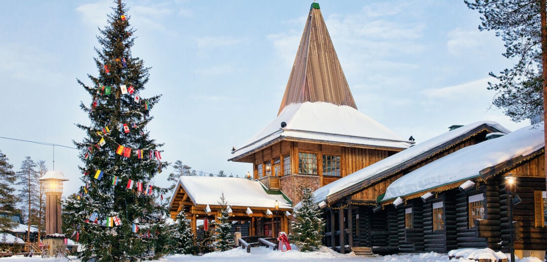 Holzhäuser in einem schneebedeckten Dorf mit geschmücktem Weihnachtsbaum
