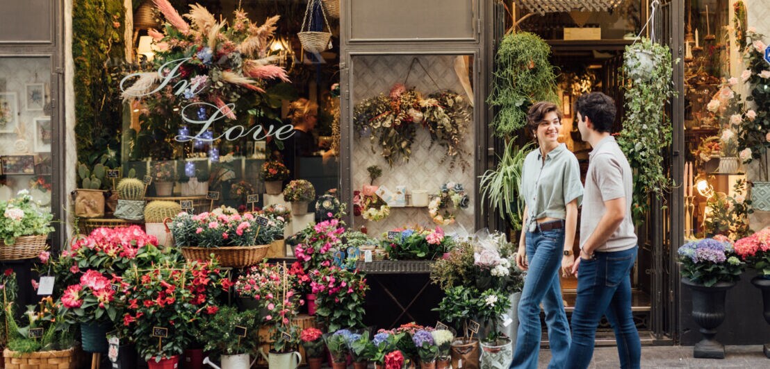 Ein Paar geht auf der Straße an einem üppig dekorierten Blumenladen vorbei.