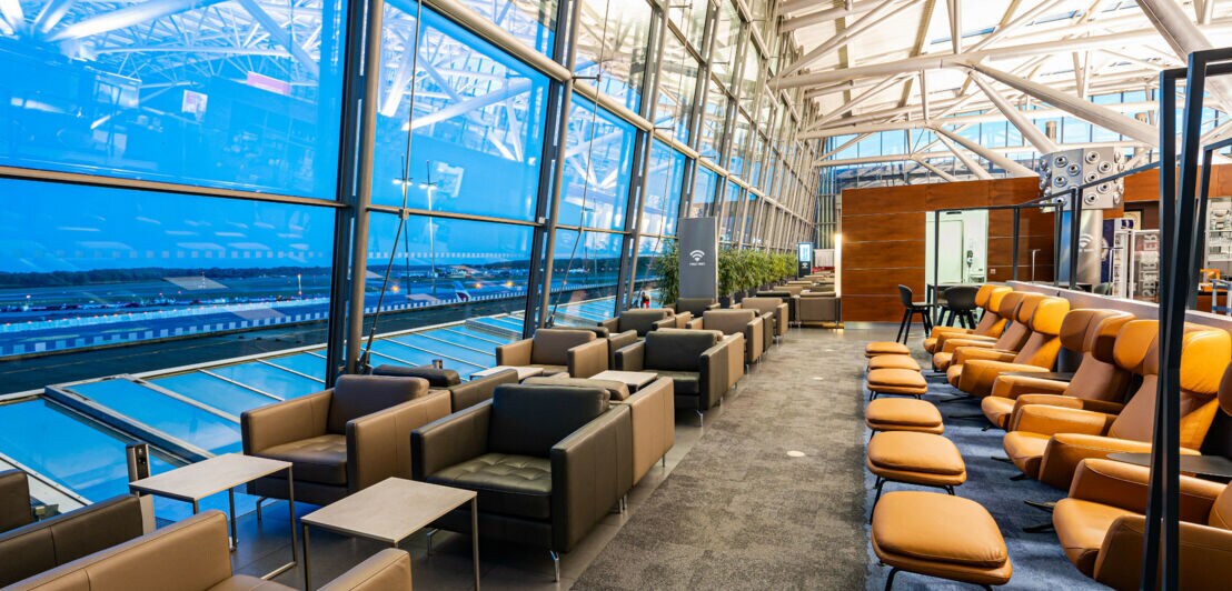 Moderne Flughafen-Lounge mit Sitzmöbeln vor Panoramafenstern mit Blick aufs Vorfeld.