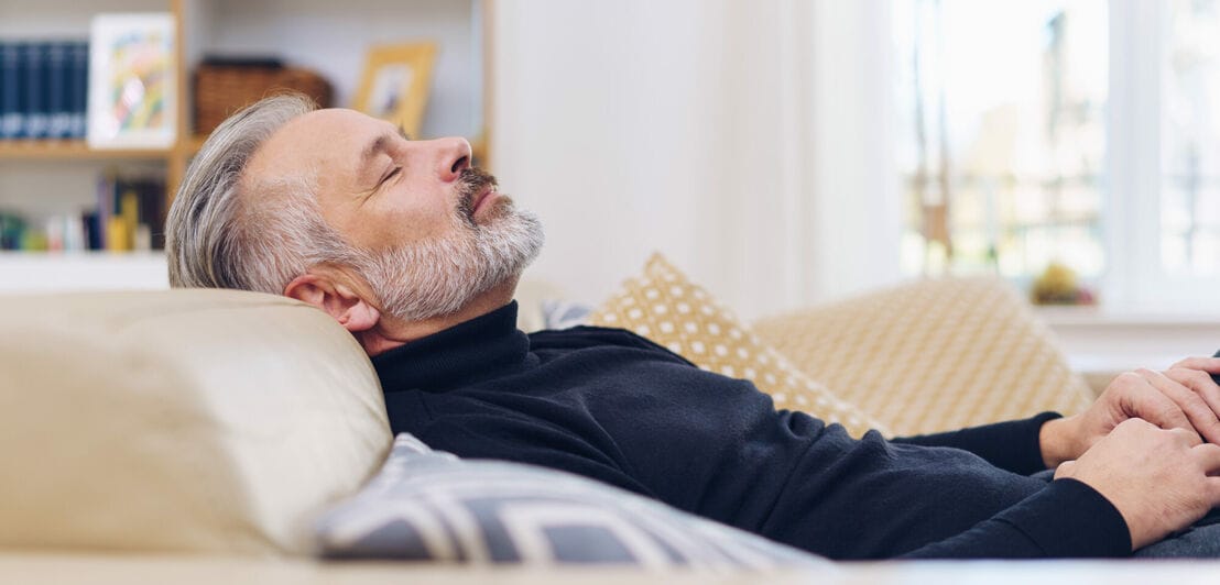 Man taking a few quiet moment to relax and have a nap lying back on a comfortable sofa at home with closed eyes
