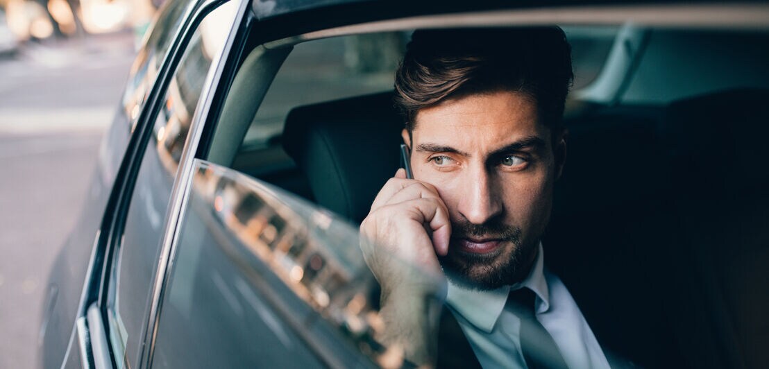 Handsome businessman talking on the mobile phone while sitting on back seat of a car.