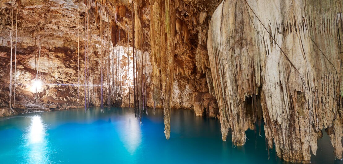 Eine Höhle mit Tropfsteindecke, die mit strahlend blauem Wasser gefüllt ist.