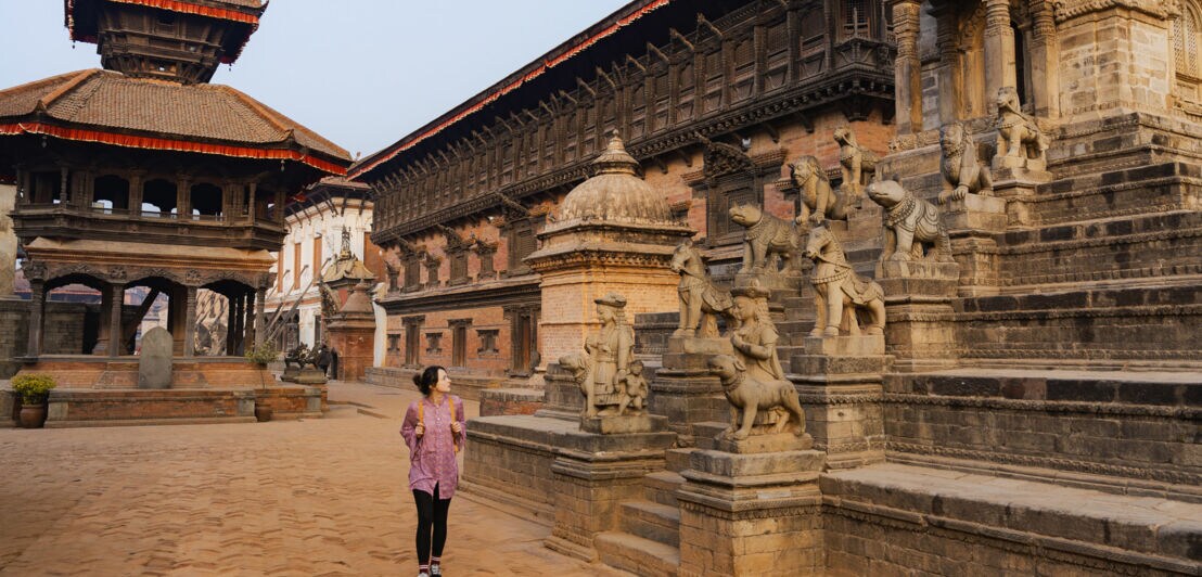 Eine Frau neben Steinskulpturen am Eingang einer Tempelanlage in Bhaktapur.