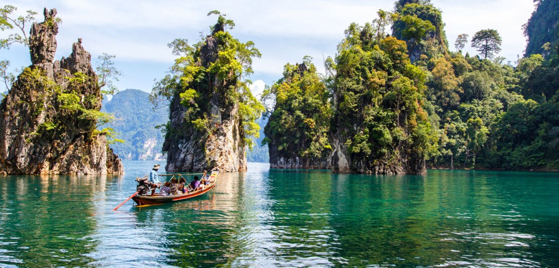Personen in einem Fischerboot auf einem See mit kleinen bewaldeten Felseninseln.
