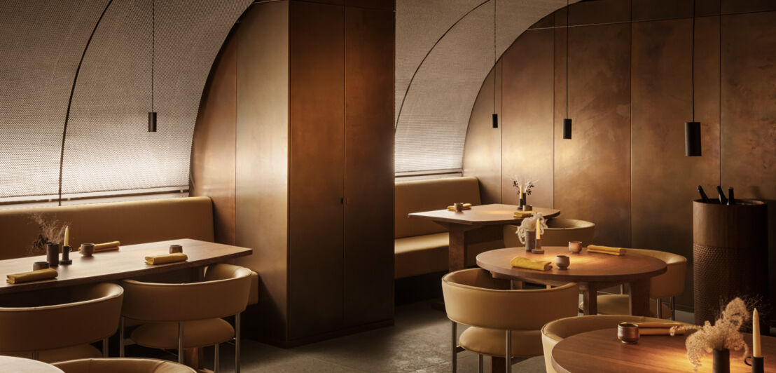 Interieur-Aufnahme eines modernen Restaurants mit Holzverkleidungen an abgerundeten Wänden und runden Holztischen bei gedimmter Beleuchtung.