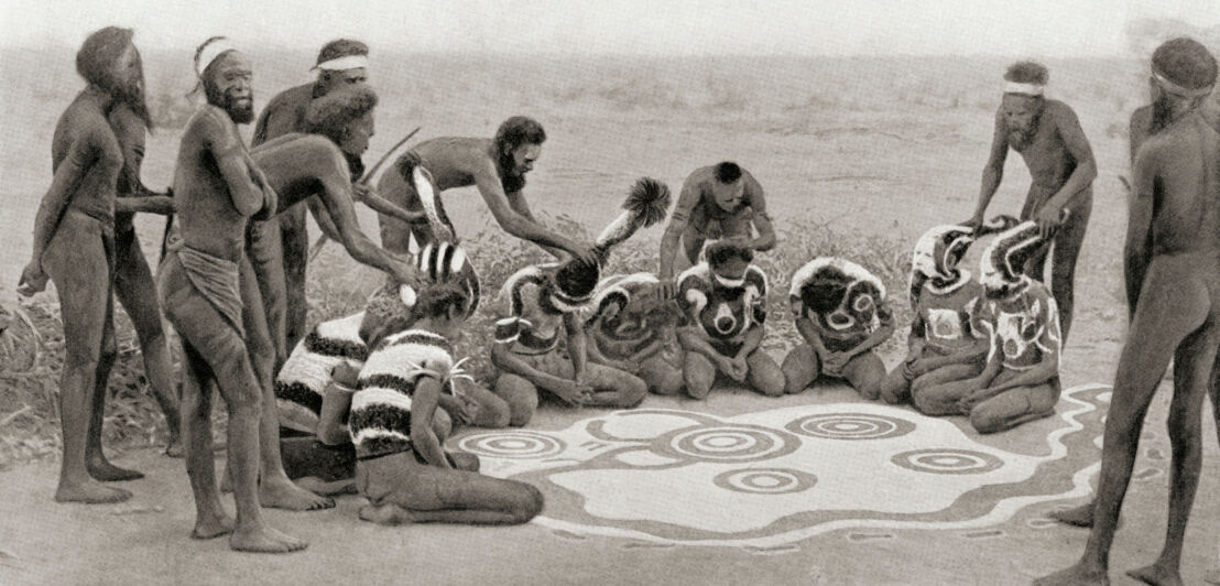 Eine Gruppe Aboriginals mit Körper- und Bodenbemalung während einer Zeremonie, Schwarzweißaufnahme.