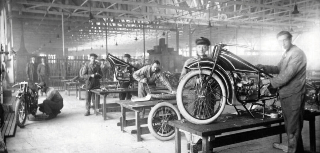 Mehrere Konstrukteure an R 32 Motorrädern von BMW in einer Industriehalle, Schwarzweißaufnahme.