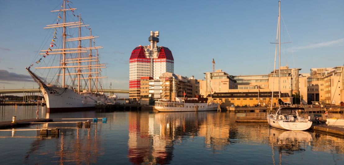 Anlagestelle im Hafen von Göteborg bei Sonnenuntergang mit verschiedenen Schiffen und dem Skanskaskrapan-Hochhaus im Hintergrund.