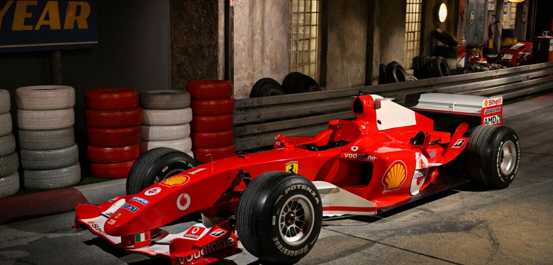 Ein roter Ferrari-Rennwagen auf einer nachgebildeten Rennstrecke in einer Ausstellung.