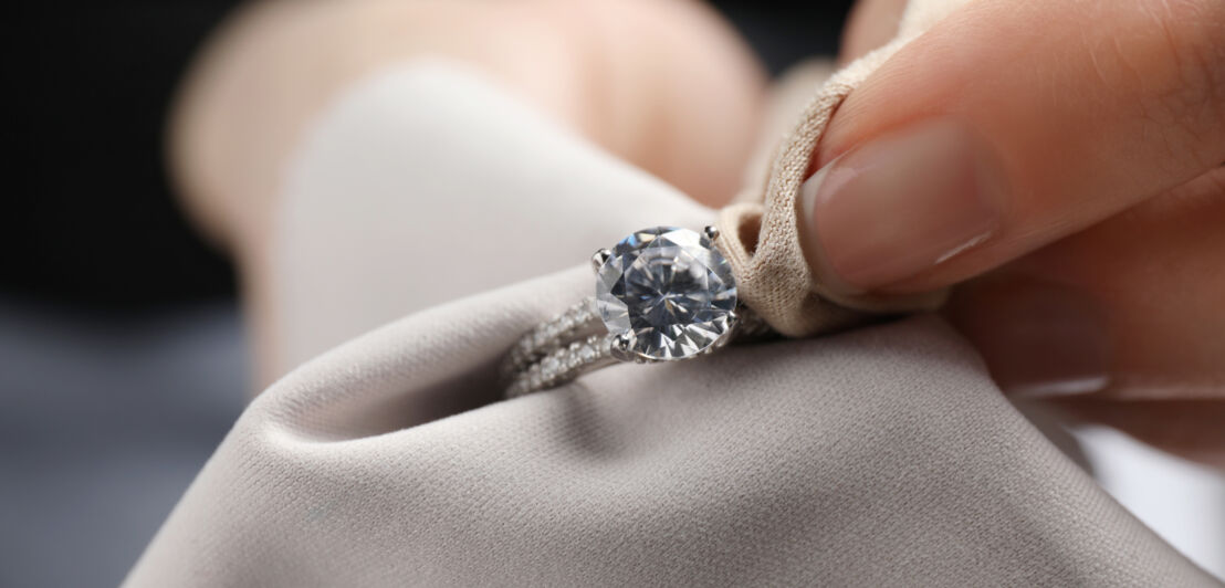 Ein Diamantring in einem hellen Tuch, das von Fingern gehalten wird.