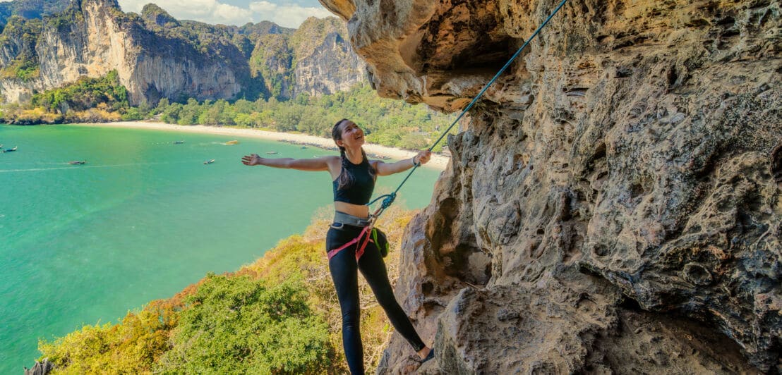 Eine Freeclimberin an einem Felsen vor Strandpanorama.