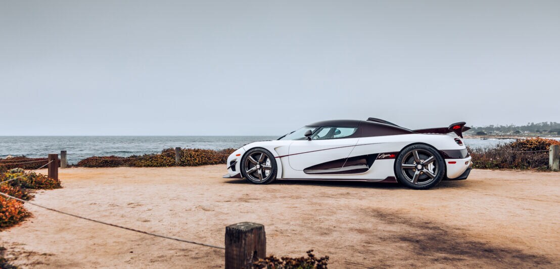 Seitenansicht eines weißen Koenigsegg Rennwagen an einer Meeresküste.