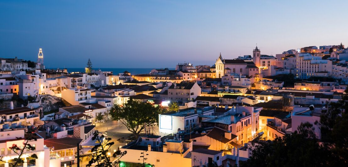 Blick auf die Skyline von Albufeira mit ihren weißen, beleuchteten Häusern bei Nacht.