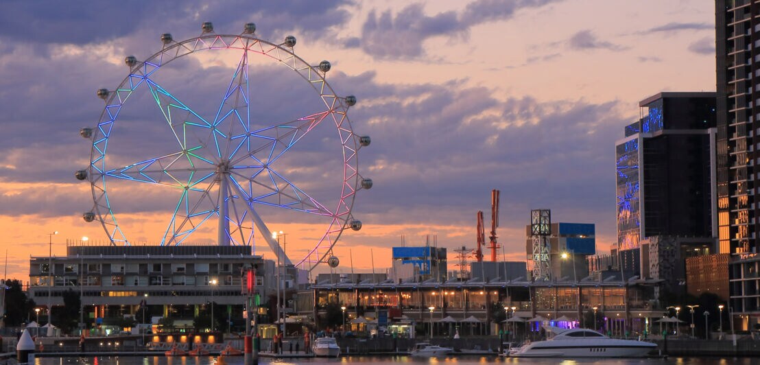 Stadtpanorama mit erleuchtetem Riesenrad an einer Waterfront bei Abenddämmerung.