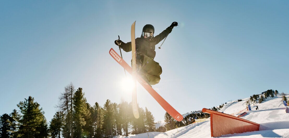 Ein Freestyle Skifahrer bei einem Sprung auf einem Parkour auf einer Skipiste.