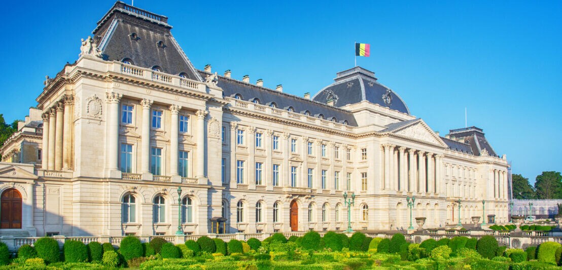 Königspalast mit belgischer Flagge, umgeben von Parkanlage.