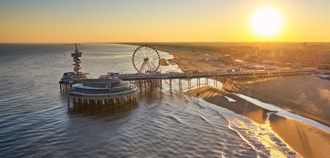 Luftaufnahme des Strandes und Riesenrads am De Pier in Scheveningen bei Den Haag bei Sonnenuntergang.