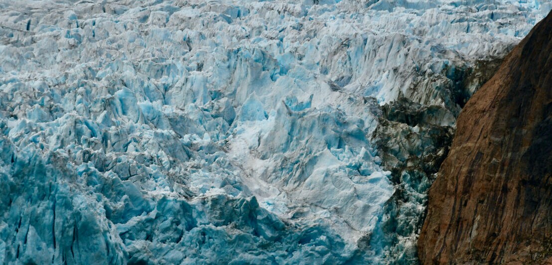 Das Bild zeigt einen riesigen Gletscher, der in das Wasser des Meeres mündet. Im Vordergrund ist ein Schlauchboot mit Gästen der Kreuzfahrt zu sehen. 