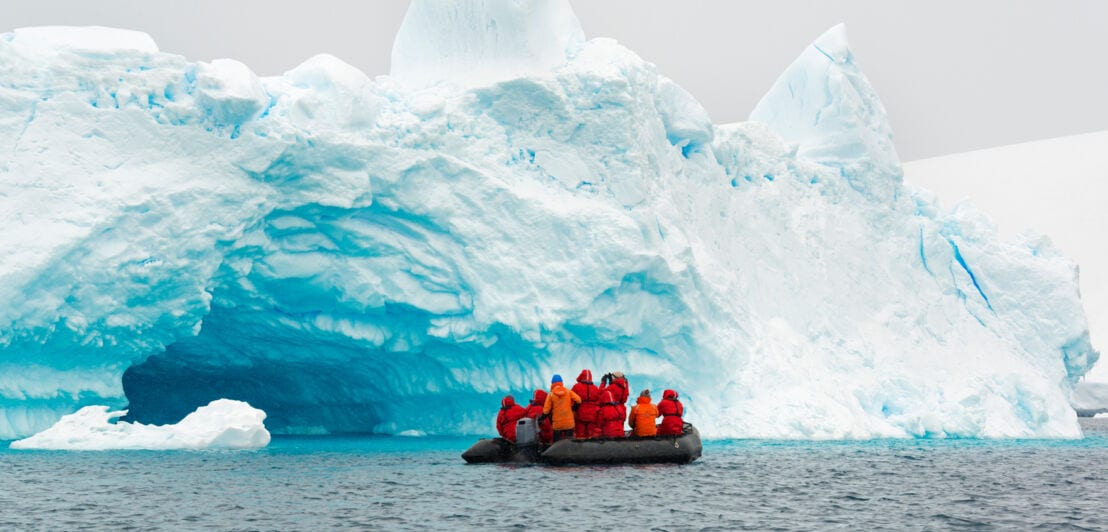 Personen auf einem Schlauchboot vor einer Eiswand im Wasser.