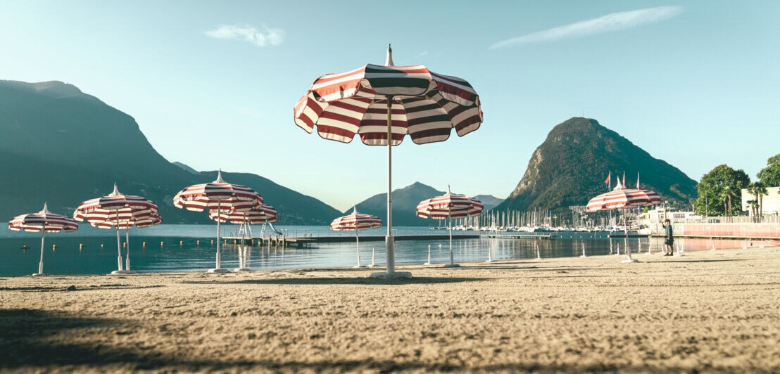 Sandstrand mit rot-weiß gestreiften Sonnenschirmen.