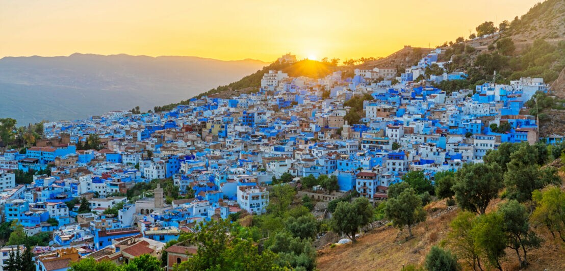 Kleinstadt mit blauen Häusern an einem Berghang bei Sonnenuntergang.