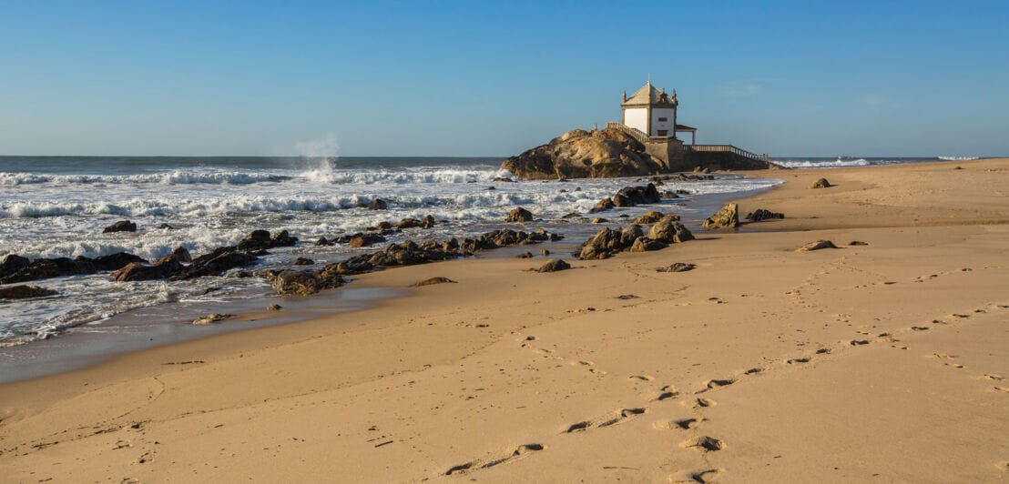 Praia da Miramar in Portugal mit Felsen, auf dem eine kleine Kapelle steht.