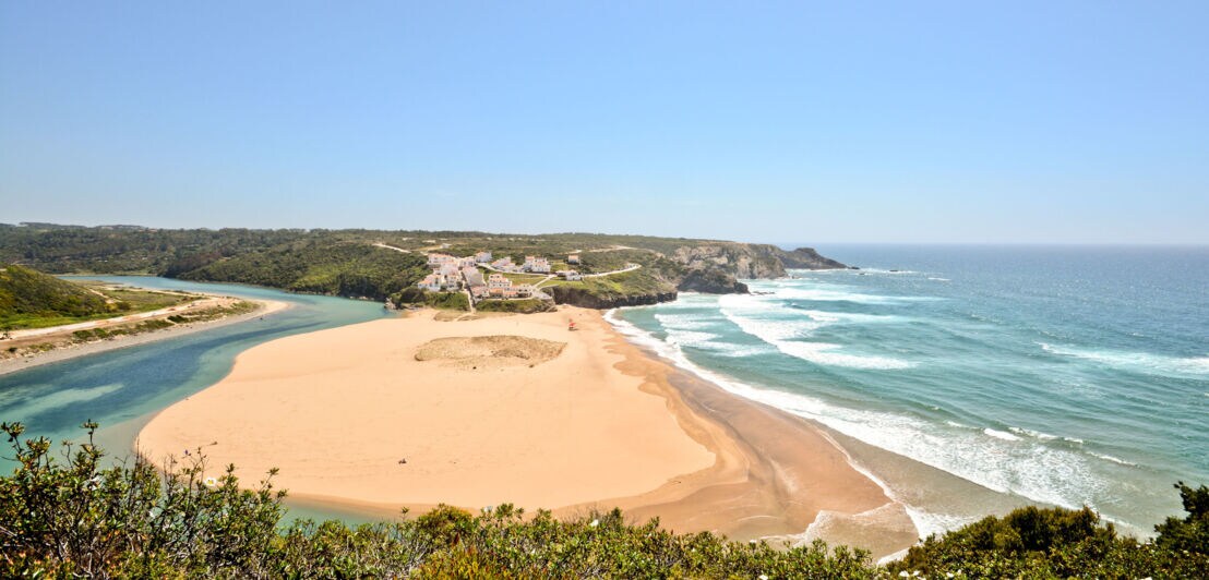 Luftaufnahme der Praia de Odeceixe mit Fluss auf der einen und Meer auf der anderen Seite.