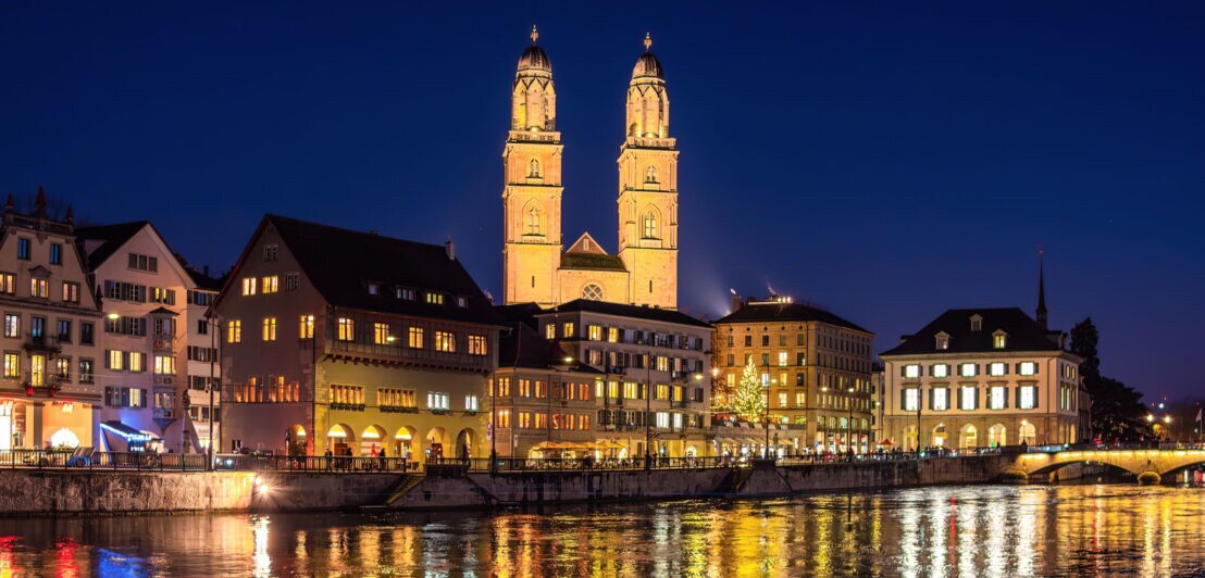 Grossmünster in Zürich bei Nacht und beleuchtet mit Häusern im Vordergrund.