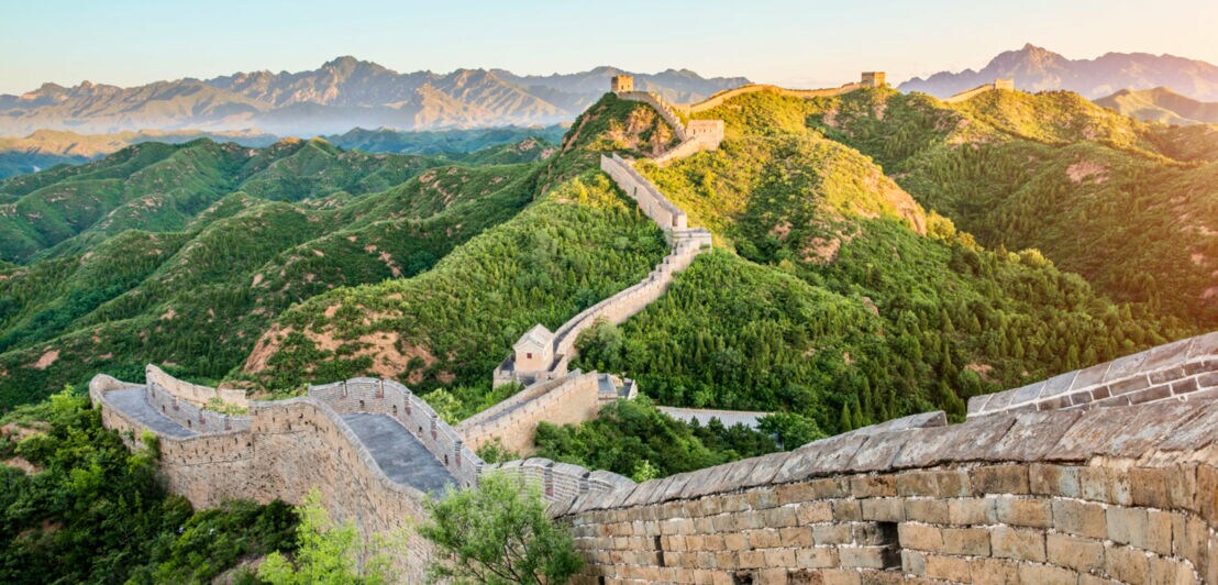 Chinesische Mauer in bewaldeter Hügellandschaft.