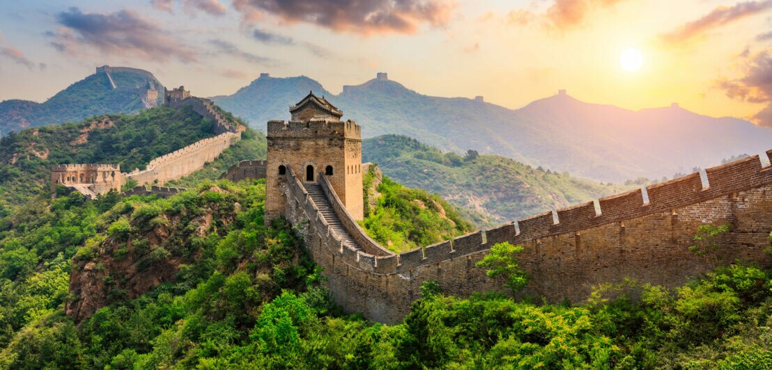 Abschnitt der Chinesischen Mauer mit Wachturm in grüner Berglandschaft.