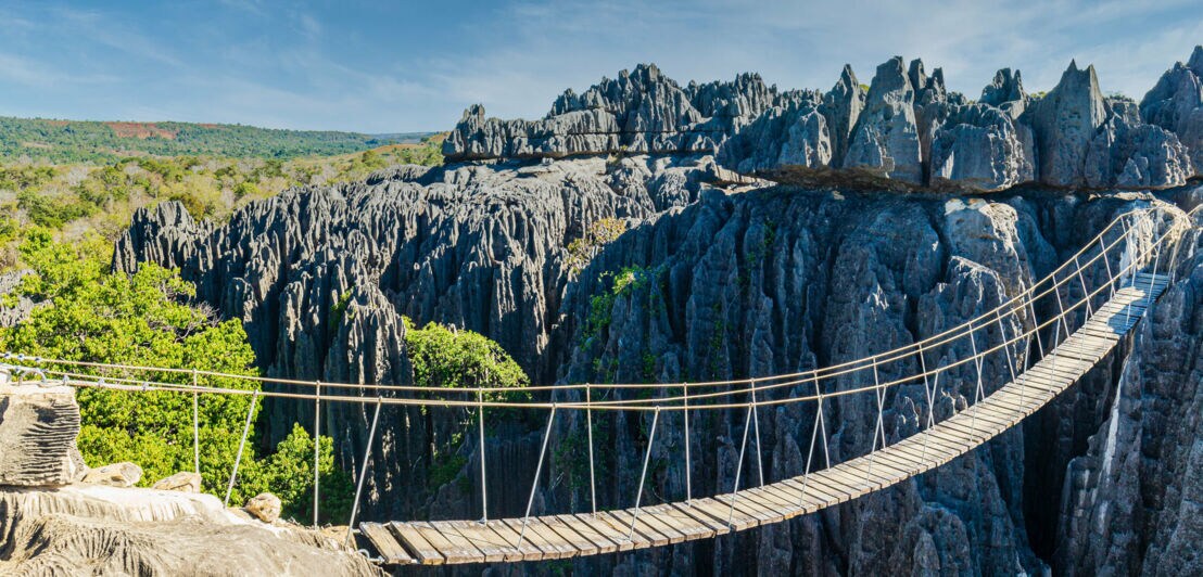 Eine Schlucht mit Hängebrücke, die zu einer Felsformation im Gebiet Tsingy de Bemaraha auf Madagaskar führt.