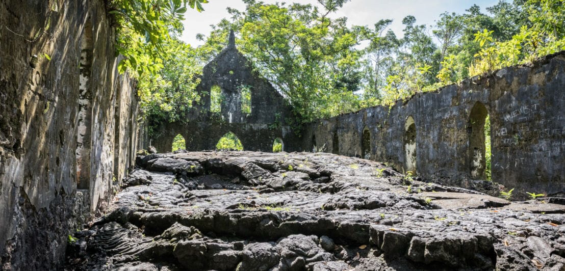 Steinruine einer Kirche mit Lavaüberresten, umgeben von tropischer Natur.