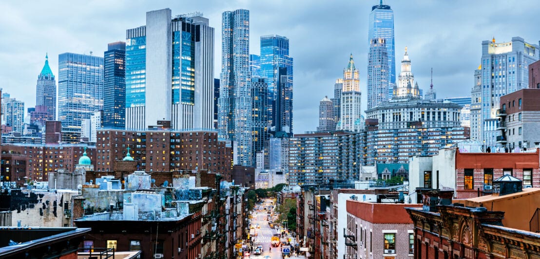 Skyline von Manhattan mit roten Backsteinhäusern vor silberglänzenden Hochhäusern im Hintergrund.