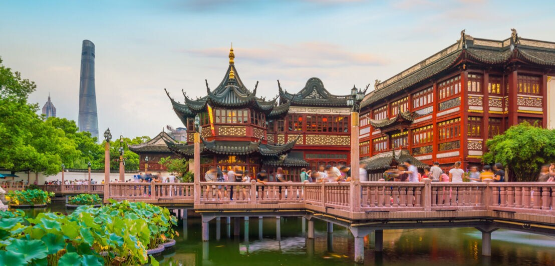 Personen auf einer Brücke vor einem chinesischen Tempel in einer Parkanlage.