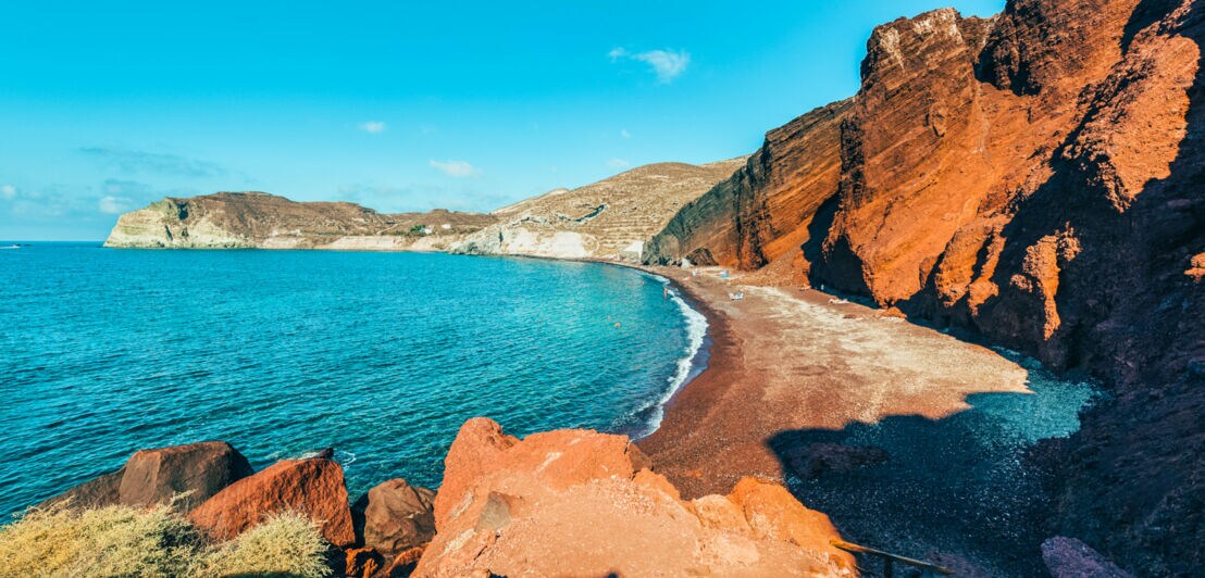 Bucht mit rotem Strand, roten Felsen und blauem Meer.